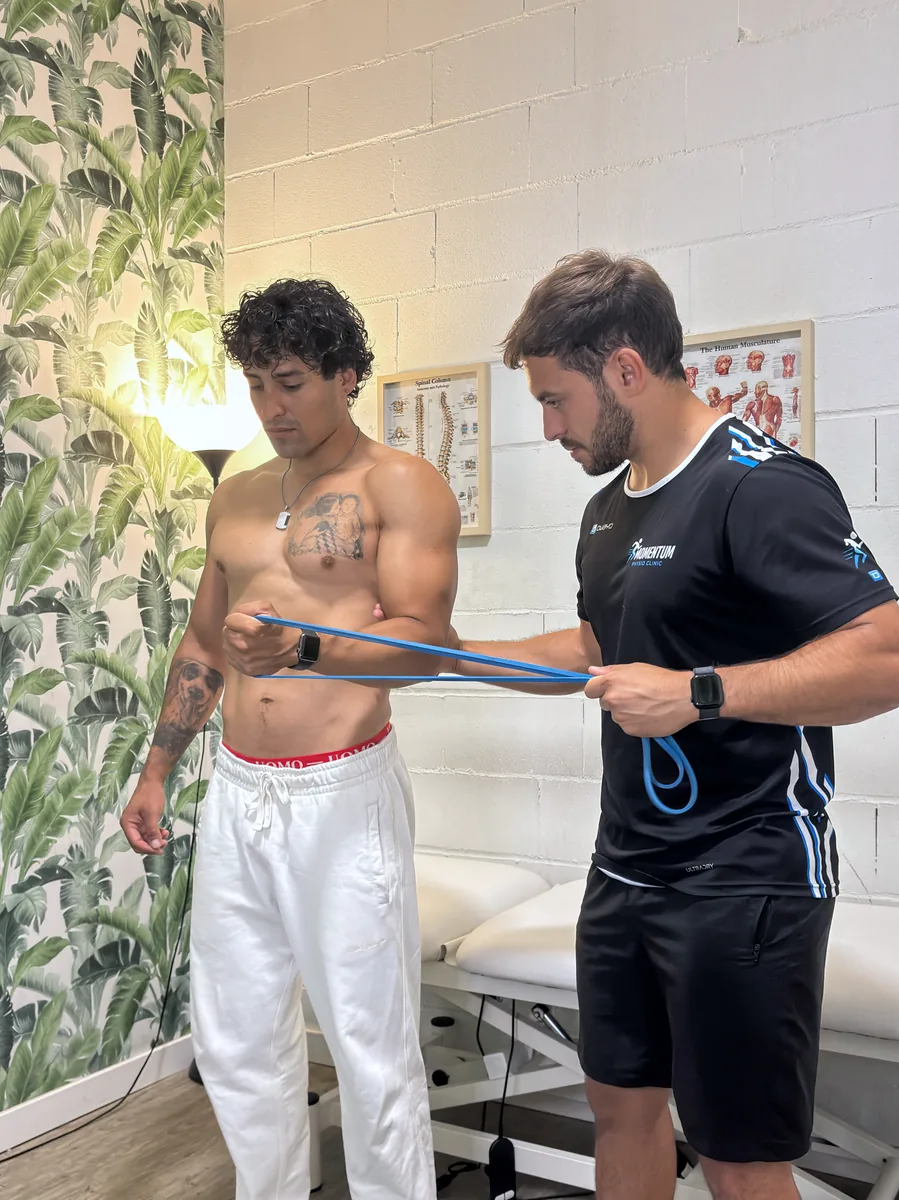Ejercicio de rotación externa de hombro con banda elástica guiado por el fisioterapeuta