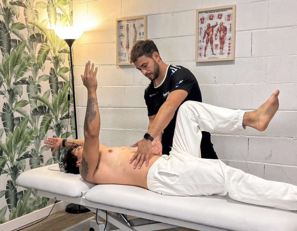 Ejercicio de control del tronco en camilla con el fisioterapeuta comprobando la estabilidad lumbar